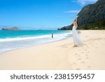 Teen girl in white dress on Hawaiian beach, arms raised in worship, feeling ocean breeze