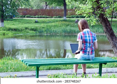 Teen Girl Working On A Laptop While Sitting On A Bench Outdoors.
Back View