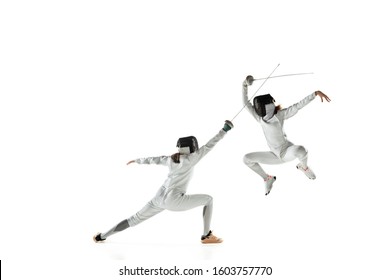 Teen girls in fencing costumes with swords in hands isolated on white studio background. Young female models practicing and training in motion, action. Copyspace. Sport, youth, healthy lifestyle.