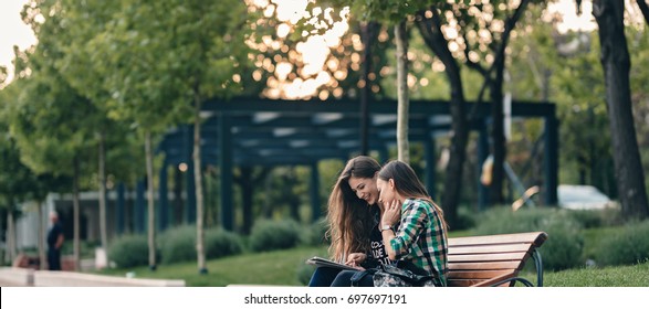 Teen Girls First Day Of School Outfit.Showing The Old Funny Pictures On Tablet.Evergreen Memories.Friendship Goals.Really Happy To See Those Old Pictures.Sitting On Wooden Bench In Park.Back To School