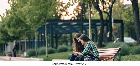 Teen Girls First Day Of School Outfit.Showing The Old Funny Pictures On Tablet.Evergreen Memories.Friendship Goals.Really Happy To See Those Old Pictures.Sitting On Wooden Bench In Park.Back To School