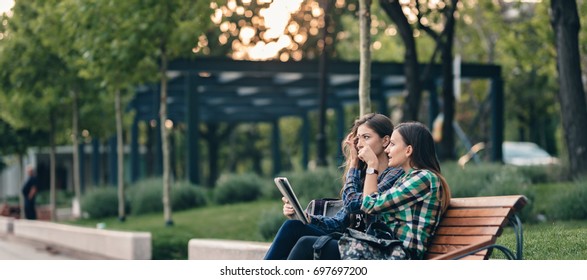 Teen Girls First Day Of School Outfit.Showing The Old Funny Pictures On Tablet.Evergreen Memories.Friendship Goals.Really Happy To See Those Old Pictures.Sitting On Wooden Bench In Park.Back To School