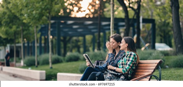 Teen Girls First Day Of School Outfit.Showing The Old Funny Pictures On Tablet.Evergreen Memories.Friendship Goals.Really Happy To See Those Old Pictures.Sitting On Wooden Bench In Park.Back To School