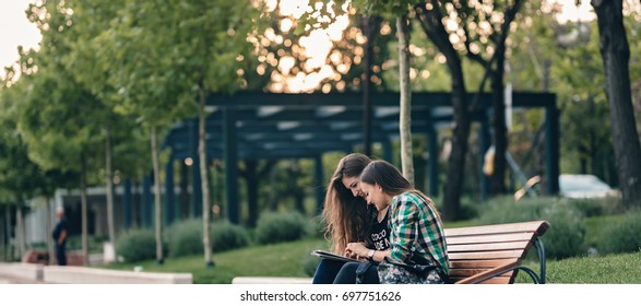 Teen Girls First Day Of School Outfit.Showing The Old Funny Pictures On Tablet.Evergreen Memories.Friendship Goals.Really Happy To See Those Old Pictures.Sitting On Wooden Bench In Park.