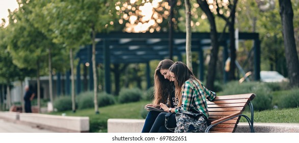 Teen Girls First Day Of School Outfit.Showing The Old Funny Pictures In Tablet.Evergreen Memories.Friendship Goals.Really Happy To See Those Old Pictures.Sitting On Wooden Bench In Park.Back To School