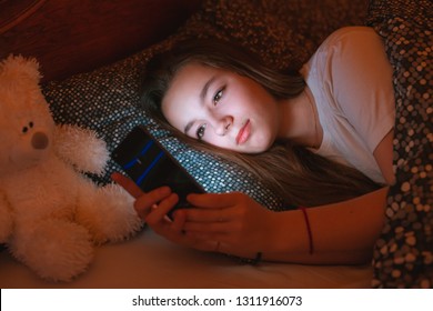 Teen Girls Lying In Bed At Night And Using Smartphone. Insomnia And The Harm Of The Smartphone Before Going To Bed. Not Healthy Sleep. Dependence On Social Networks In Adolescents.