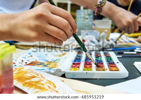 Teen girls painting pictures together. Close up view of their hands.                                