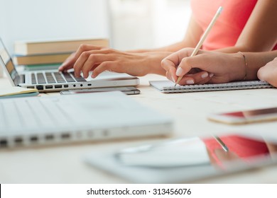 Teen Girls Studying At Desk And Doing Homeworks, One Is Using A Laptop And The Other One Is Writing On A Notebook, Education Concept, Unrecognizable People