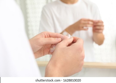 Teen guy using acne healing patch near mirror indoors, focus on hands