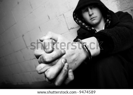 teen in handcuffs, young teen against wall with dirty hands and handcuffs, converted to black and white with slight added grain. focus on cuffs.