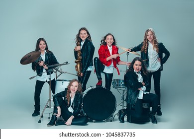 Teen Music Band Performing In A Recording Studio. The Group Of Girls Standing Together And Posing At Camera. Studio Portrait Of Young Attractive Fashion Caucasian Teen Girls Dressed Inblack Leather