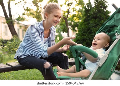 Teen nanny with cute baby in stroller playing in park