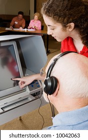 Teen Poll Worker Assists Senior Voter On Touch Screen Machine.