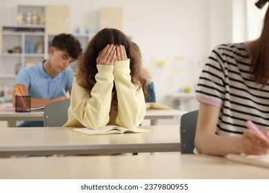 Teen problems. Lonely girl sitting separately from other students in classroom - Powered by Shutterstock