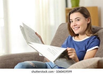 Teen Reading A Newspaper Looking At Camera Sitting On A Couch In The Living Room At Home