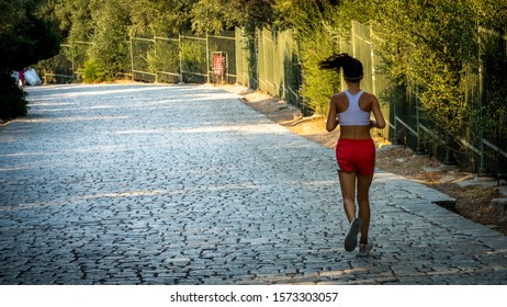 Teen In Red Shorts And White Tanktop Jogging On Cobblestone Road In Athens Greece