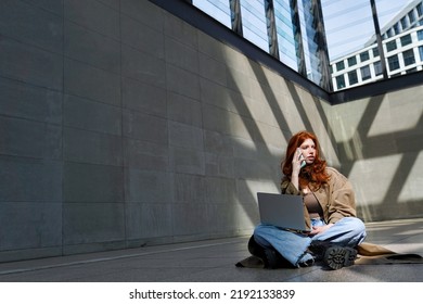 Teen Redhead Hipster Girl Student Talking On Cell Phone Using Laptop Computer Modern Technology Connected Devices In City Urban Location Outdoors.