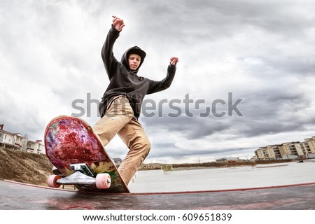 Teen skater in a hoodie sweatshirt and jeans slides over a railing on a skateboard in a skate park