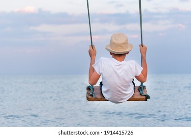 Teen In Straw Hat Riding On Rope Swing Over The Water. Swing Against The Sky And The Sea.