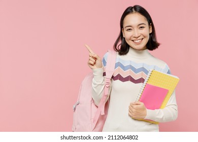 Teen student girl of Asian ethnicity wear sweater backpack hold books point index finger aside on workspace area isolated on pastel plain light pink background Education in university college concept - Shutterstock ID 2112064802