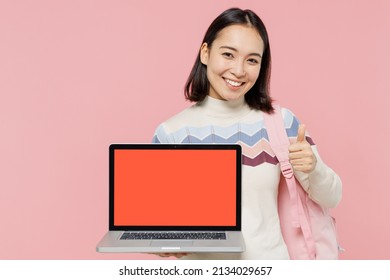 Teen Student Girl Of Asian Ethnicity In Sweater Backpack Hold Books Hold Use Work On Laptop Pc Computer With Blank Screen Workspace Area Show Thumb Up Isolated On Pastel Plain Light Pink Background