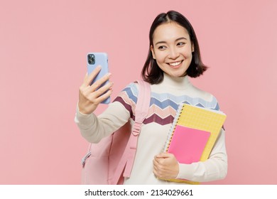 Teen Student Girl Of Asian Ethnicity In Sweater Backpack Hold Books Doing Selfie Shot On Mobile Cell Phone Isolated On Pastel Plain Light Pink Color Background Education In University College Concept