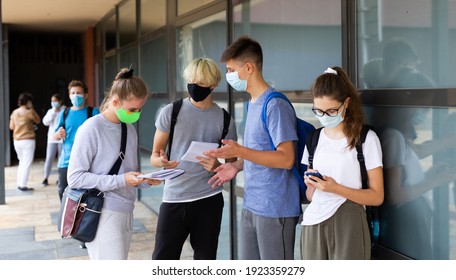 Teen students in medical face masks standing with workbooks in schoolyard during break in lessons. Concept of back to school after lockdown - Shutterstock ID 1923359279