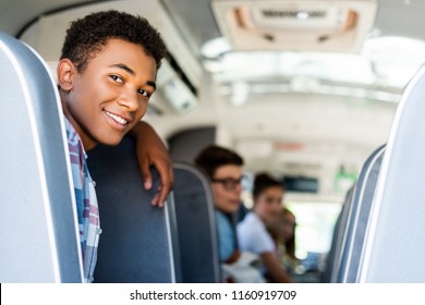 Teen Students Sitting At School Bus And Looking Back At Camera