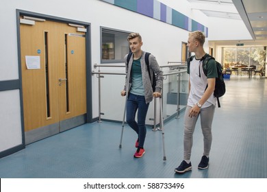 Teen students are walking down the school hall together. They have left lesson early, as one of the boys is on crutches and requires assistance from his friend. 