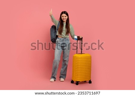 Teen Travel Programs. Positive Young Girl With Tickets And Suitcase Showing Thumb Up Gesture While Posing On Pink Studio Background, Cute Female Teenager Enjoying Travelling, Full Length, Copy Space