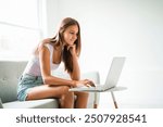 The teen using laptop sit on sofa in the living room.