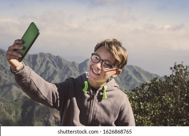 Teen Using Smartphone Outdoors In Mountain. Young Boy Taking Selfie With Mobile Phone During Holiday. Making Video Call With Cell Phone App To Communicate With Friends. Youth, Fun, Lifestyle Concept