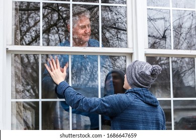 Tee, der Senioren besucht, die zu Hause unter Quarantäne stehen, Hände durch das Fenster berührt, Hauptfokus auf den Hut des Jungen und Mann im Fenster