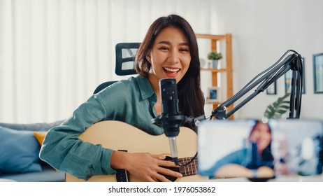 Teenage Asia girl influencer play guitar music use microphone record with smartphone for online audience listen at home. Female podcaster make audio podcast from her home studio, Stay at home concept. - Powered by Shutterstock