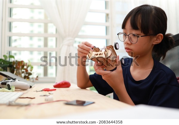 Teenage Asian\
girl building a solar toy car through online e-learning at home.\
Student doing school project or learning science through video call\
with teacher. Soft focus\
image.