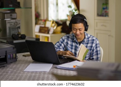 Teenage Of Asian People Writing A Note While Learning From Online Lesson At Home. Studying At Home And Self Study Concept.