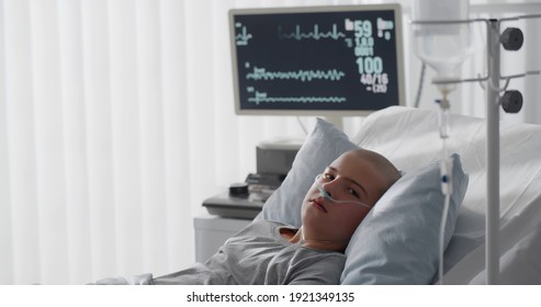 Teenage bald boy lying in hospital with oxygen tube. Side view of kid patient in oncology clinic resting in bed having chemotherapy treatment in ward