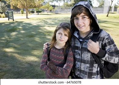 Teenage boy (15 years) with arm around younger sister (11 years), with bookbags at school