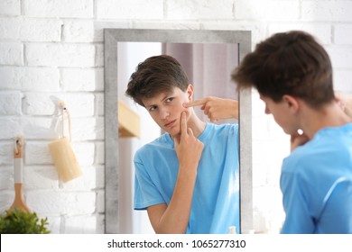 Teenage boy with acne problem looking in mirror at home