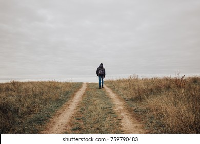 Teenage boy with backpack walking away on the rural road.
