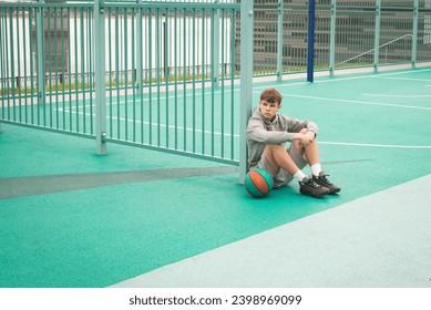 Teenage boy basketball player sitting alone at sportground - Powered by Shutterstock