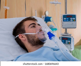 Teenage boy with a beard and an oxygen mask stays in a hospital room
