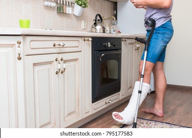 A Teenage Boy With A Broken Foot Alone At Home In The Kitchen Makes Tea. Leg In A Cast. Disease.