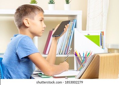 Teenage Boy Doing Homework, Using Cell Phone Recording And Send A Voice Message, Making Voice Call, Using Learning Application. Online Learning, Remote Education At Home