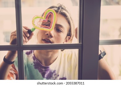 Teenage boy drawing and coloring heart shape on glass of door using marker at home. Caucasian boy drawing heart shape symbol on window. Teenager writing symbolic message of love on glass.