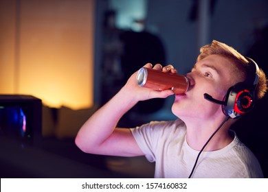 Teenage Boy Drinking Caffeine Energy Drink Gaming At Home Using Dual Computer Screens At Night