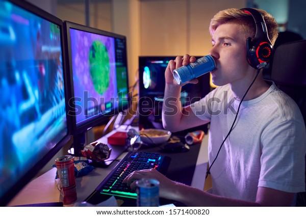 Teenage Boy Drinking Caffeine\
Energy Drink Gaming At Home Using Dual Computer Screens At\
Night