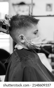 A teenage boy gets a haircut in a barbershop during a pandemic, a haircut in the salon, a client and a hairdresser in masks, a baby haircut with scissors.