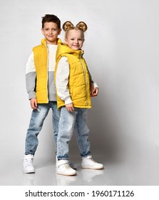 teenage boy and girl posing against a light background, children are dressed in yellow puffy sleeveless zipper vests and jeans. urban teen fashion