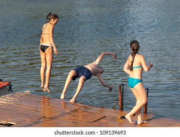 Teenage Boy And Teenage Girls Jumping Into The River From Old Dock.